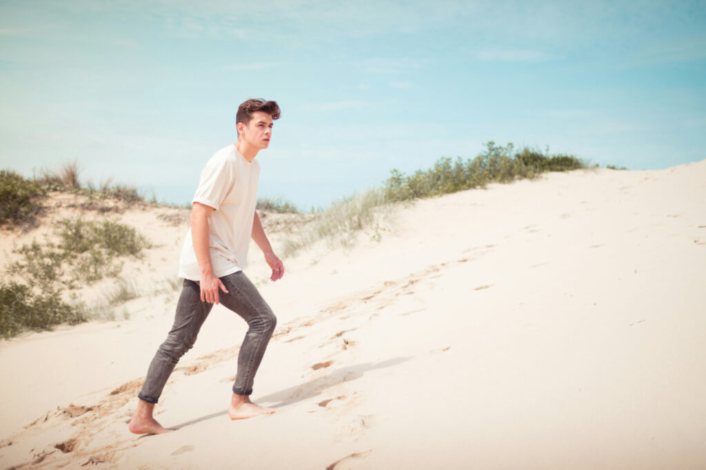 A man walks up a sand dune