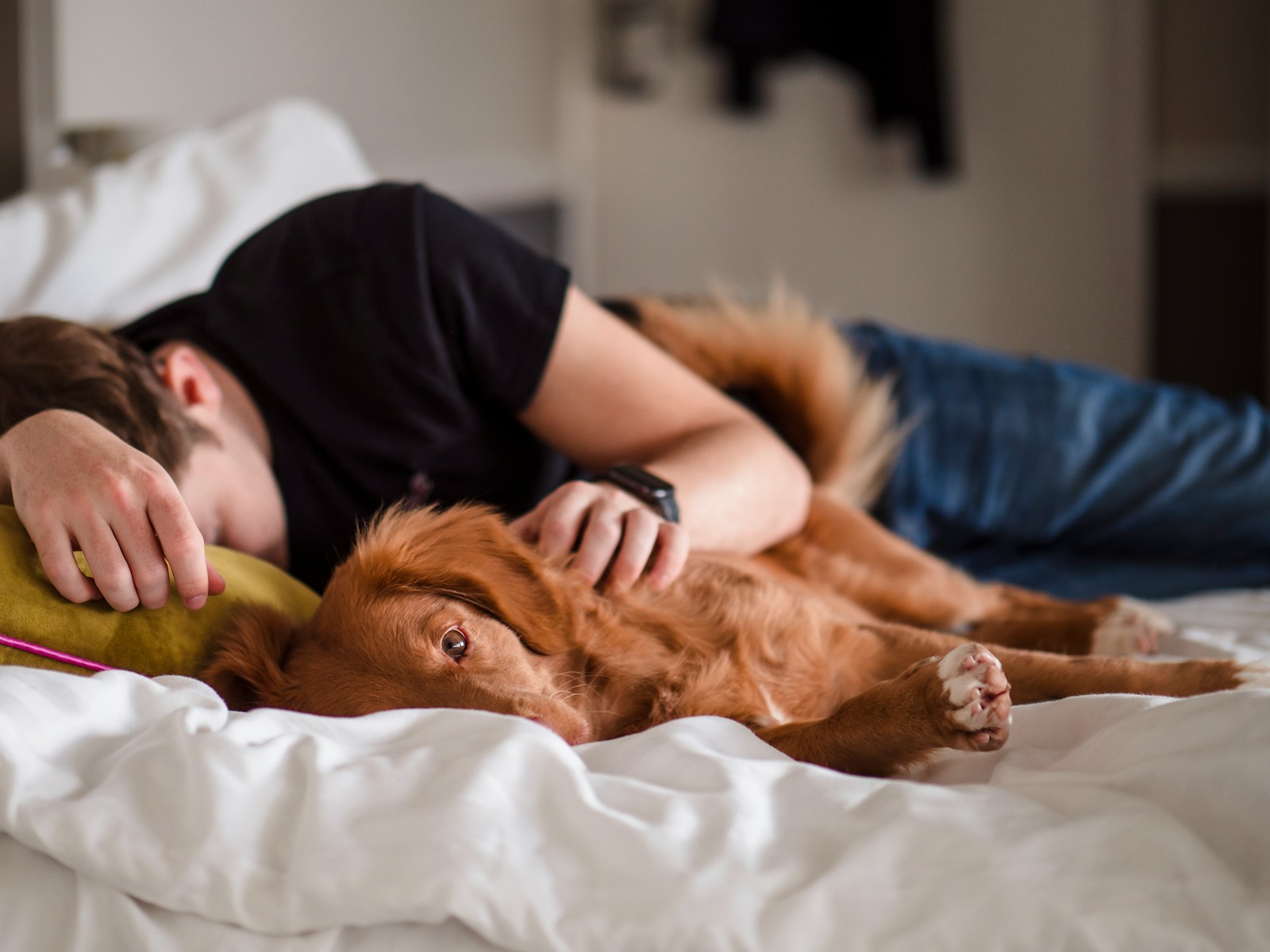 person in black shirt lying on bed with a dog