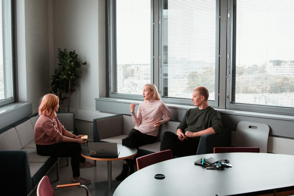 Two women sit on a sofa across from a therapist. One of the women is speaking.